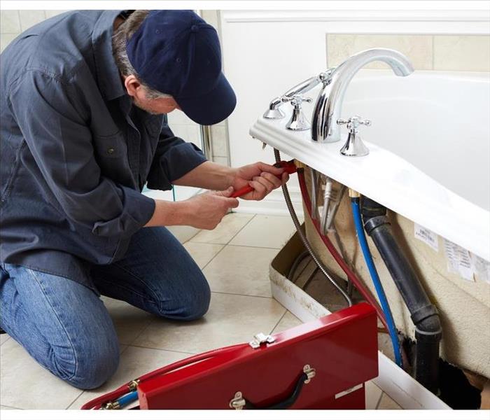 A bathtub leak is being repaired by a plumber. 